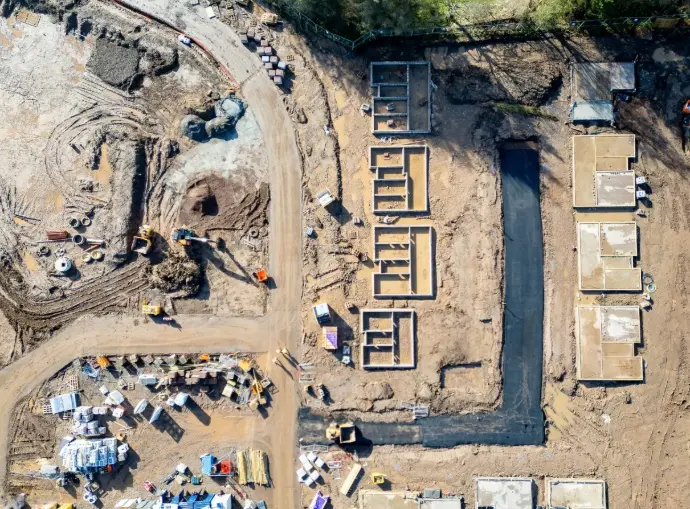 Vista aérea cenital de una nueva urbanización en fase de construcción en Málaga, mostrando los cimientos de múltiples viviendas ya definidos, maquinaria en el terreno, materiales de construcción organizados y caminos de tierra que delinean las futuras calles. Esta imagen es ideal para promotoras inmobiliarias y empresas constructoras en Málaga que deseen documentar el avance de sus proyectos de urbanización. Los servicios de dron permiten realizar un seguimiento exhaustivo del desarrollo de nuevas áreas residenciales, facilitando la planificación, el control de calidad y la promoción visual de los terrenos y futuras propiedades en la Costa del Sol.