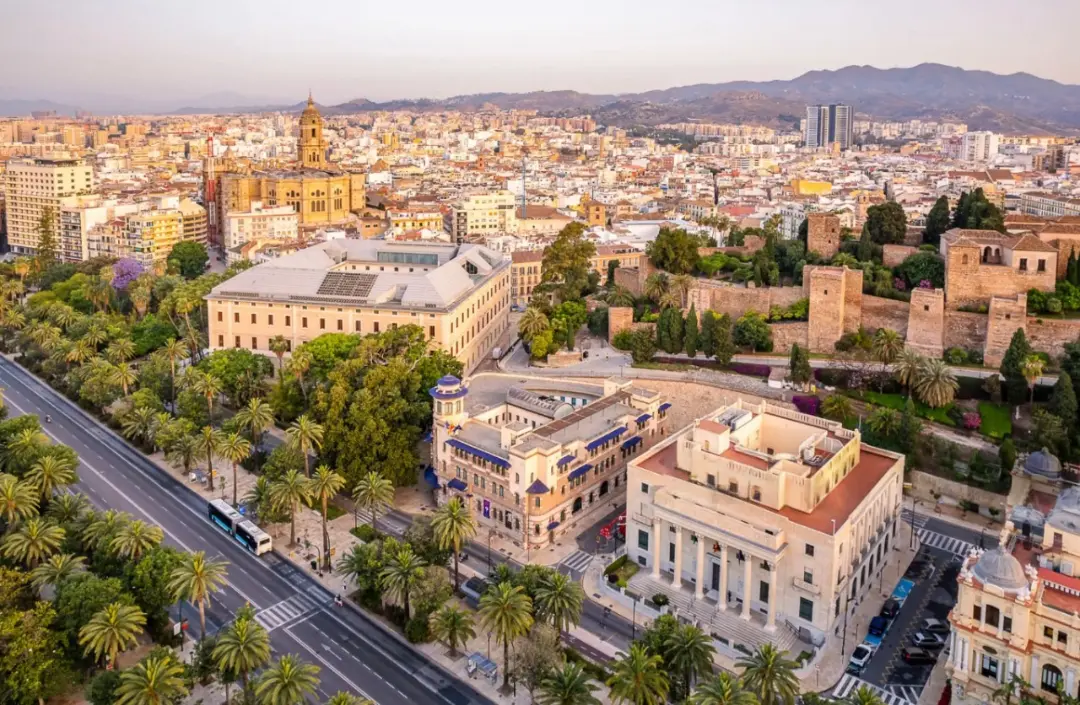 Vista aérea panorámica del centro histórico de Málaga, destacando el edificio del Ayuntamiento y sus alrededores, la Alcazaba, el Parque de Málaga y parte del Paseo de los Curas, con la ciudad extendiéndose hacia las montañas al fondo. Esta imagen es perfecta para servicios de fotografía y vídeo aéreo profesional en Málaga, ideal para promoción turística, proyectos urbanísticos, eventos culturales o reportajes visuales que requieran una perspectiva única de los lugares más emblemáticos de la capital.