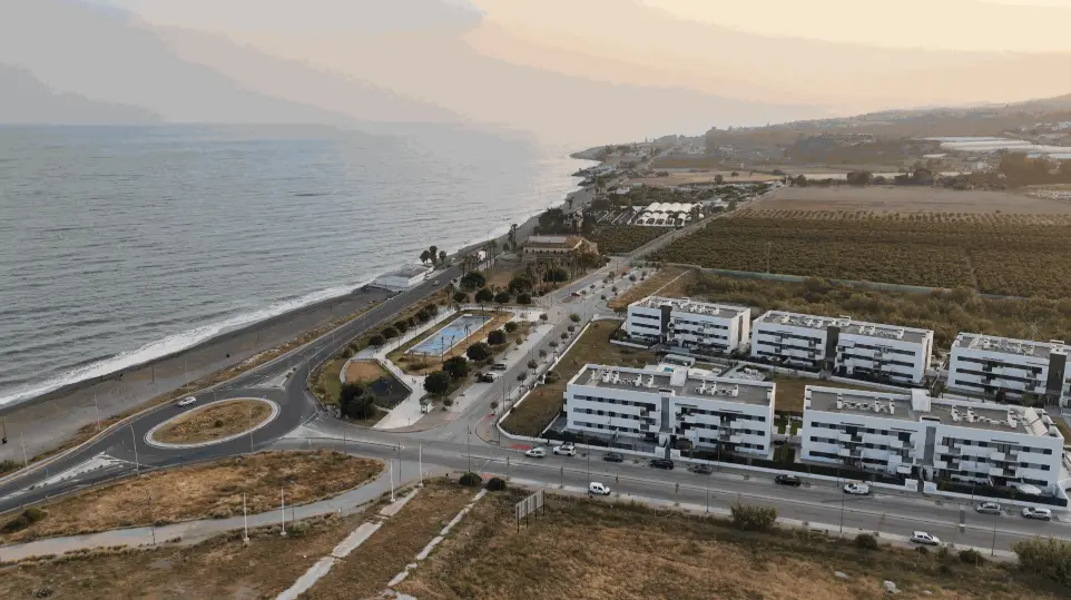 Playa Almayate dron, costa Málaga aérea, urbanizaciones Axarquía, vídeo dron inmobiliaria Vélez-Málaga, fotografía aérea litoral Málaga. Vista aérea de la costa de Almayate, Málaga, mostrando la playa, una carretera litoral serpenteante con una rotonda, un carril bici, y un complejo de edificios residenciales modernos. La imagen capta el ambiente tranquilo de una zona costera con campos de cultivo en el interior. Es ideal para promocionar el atractivo de las playas y urbanizaciones de la Axarquía malagueña, ofreciendo servicios de fotografía y vídeo con drones para el sector inmobiliario en Almayate, Vélez-Málaga y toda la costa este, así como para la promoción turística de la zona.