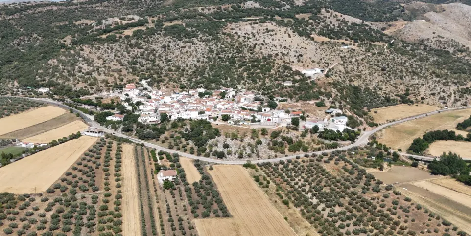 Pueblo blanco Málaga dron, fotografía aérea rural, vistas aéreas pueblos Axarquía, vídeo turístico interior Málaga, dron patrimonio rural. Impresionante vista aérea de un típico pueblo blanco de Málaga, enclavado en un paisaje rural montañoso, rodeado de campos de olivos, tierras de cultivo y carreteras serpenteantes. La imagen muestra la distribución de las casas, sus tejados y el entorno natural que lo abraza. Esta fotografía es ideal para servicios de fotografía y vídeo aéreo para el turismo rural en la provincia de Málaga, la promoción de pueblos con encanto, proyectos de desarrollo local, o para el sector inmobiliario que busque destacar propiedades en entornos pintorescos de interior.
