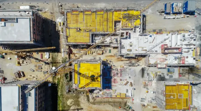 Vista aérea cenital de una gran obra de construcción en Málaga, mostrando múltiples estructuras en diferentes fases de edificación, andamios, grúas y tejados en proceso de instalación. La imagen resalta el dinamismo y la complejidad de un proyecto de gran envergadura. Es ideal para empresas constructoras y promotoras inmobiliarias en Málaga que requieran un seguimiento detallado y preciso del avance de sus obras, inspección de tejados y cubiertas, y control de calidad. Los drones permiten obtener una perspectiva global y detallada para la planificación y gestión de grandes construcciones en la provincia de Málaga.