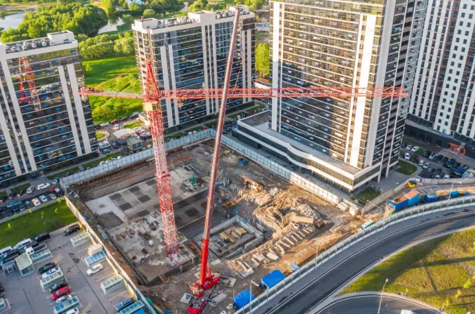 Impresionante vista aérea de un nuevo desarrollo de construcción en Málaga, mostrando los cimientos de un edificio en proceso, flanqueado por altas torres de apartamentos ya terminadas y una gran grúa roja dominando el centro del solar. La imagen ofrece una perspectiva única del crecimiento urbano en la ciudad. Es ideal para promotoras inmobiliarias, constructoras y fondos de inversión en Málaga que necesiten un seguimiento exhaustivo y documentación visual del progreso de sus proyectos residenciales y urbanísticos, facilitando la gestión y la promoción de nuevas viviendas en la capital y la Costa del Sol.