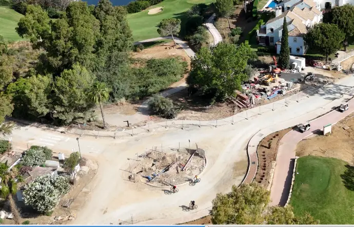 Vista aérea de una zona en desarrollo o renovación en un entorno residencial con campos de golf en Málaga, mostrando una rotonda en construcción o remodelación, con maquinaria y materiales de obra visibles. Alrededor, se aprecian viviendas, zonas verdes y parte de un campo de golf. Esta imagen es ideal para empresas de construcción, promotoras o ayuntamientos en la provincia de Málaga que necesiten un seguimiento y documentación aérea de obras viarias, paisajismo o desarrollo de urbanizaciones, ofreciendo una perspectiva detallada del progreso de proyectos en entornos complejos.