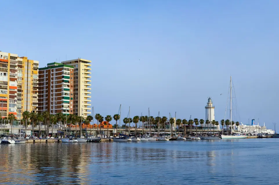 Puerto Málaga dron, fotografía aérea costa, faro La Farola Málaga, marina vista aérea, servicios audiovisuales Málaga capital. Vista panorámica del puerto de Málaga, mostrando la vibrante combinación de edificios residenciales y hoteleros, palmeras, embarcaciones amarradas en la marina, y el icónico faro de La Farola, con el mar Mediterráneo en primer plano. Esta imagen, aunque nombrada "torremolinos-dron.jpg", representa el puerto de Málaga capital. Es ideal para servicios de fotografía y vídeo aéreo promocional en el ámbito turístico y portuario de Málaga, destacando la belleza de su costa, la infraestructura de su puerto o la vida urbana de la ciudad, perfecta para el sector inmobiliario y de hostelería en la Costa del Sol.